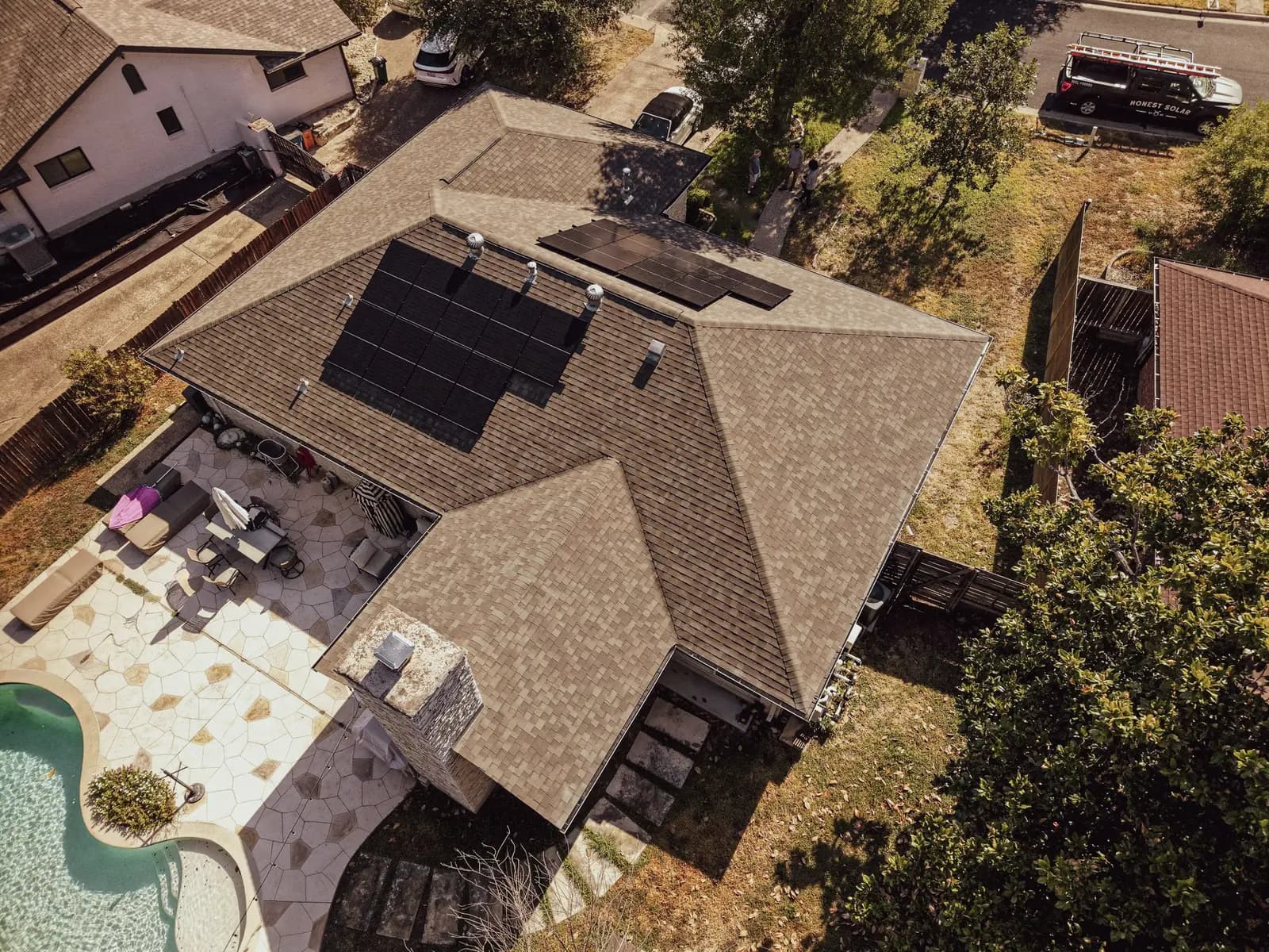 Aerial view of a completed Honest Solar residential install, two roof-mounted arrays and the Honest Solar truck at the curb