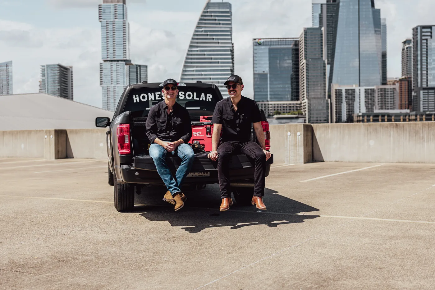 Honest Solar founders Jonathan and Patrick on the tailgate of their truck, downtown Austin skyline behind