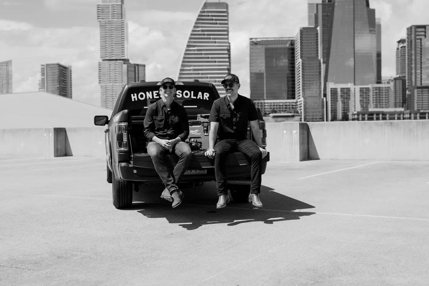 Honest Solar founders Jonathan and Patrick on the tailgate of their truck, downtown Austin skyline behind